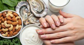 Bàn tay với móng tay khỏe mạnh đặt cạnh đĩa thực phẩm giàu kẽm và canxi như hàu, các loại hạt và rau xanh.
